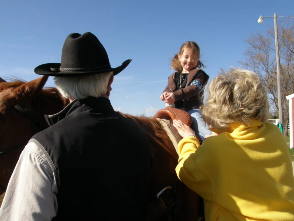 A little girl in on a saddle while two older people look at her.