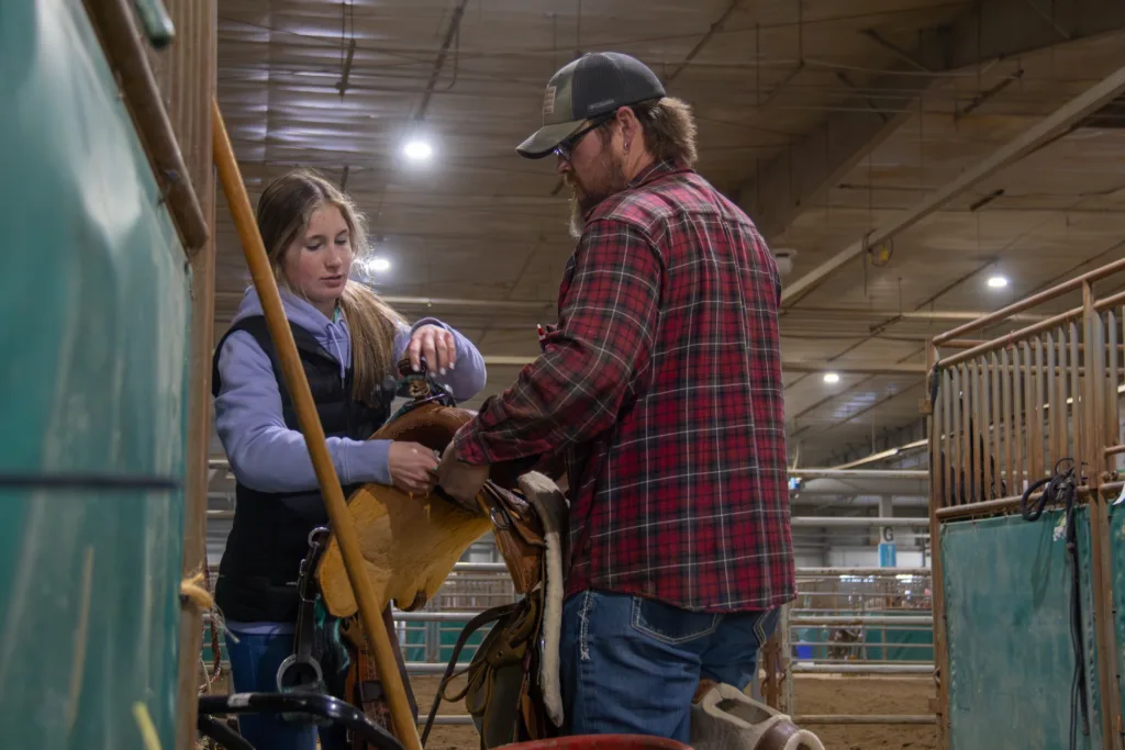 A young girl and her father put away a saddle.
