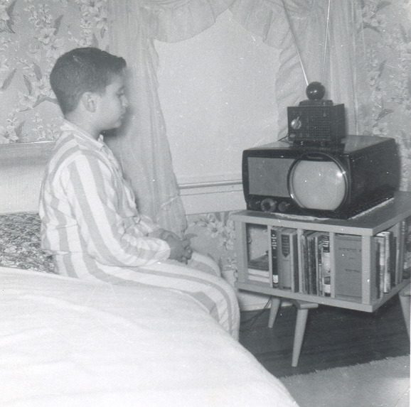 1955 photo of Harry Friedman as a boy, watching TV while sitting on the edge of a bed