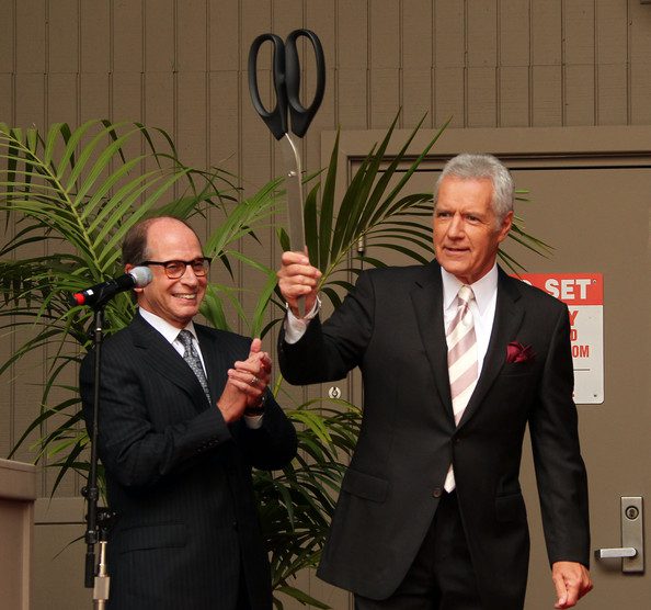 Harry Friedman, left, claps while Alex Trebek holds a giant pair of scissors.