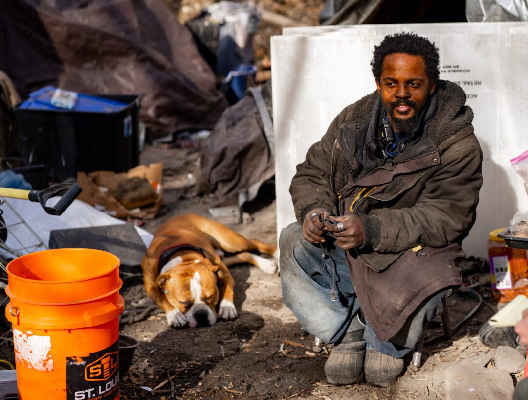 Roland Busby sits in front of his tent with his dog Capone at a homeless encampment near 40th and Decatur Streets on Feb. 22, 2024. Photo by Abiola Kosoko for the Flatwater Free Press